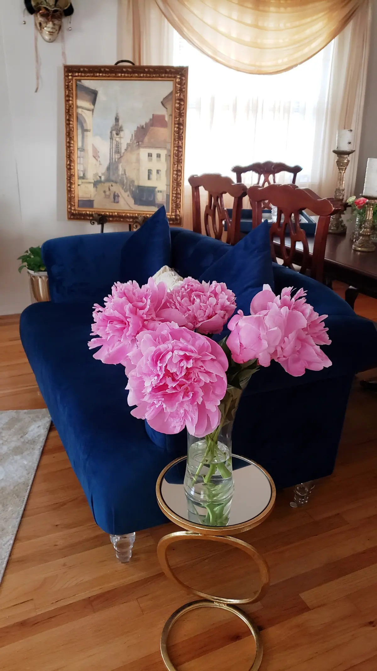 Pink peonies on gold table beside navy velvet loveseat — styled by Renata Glaz